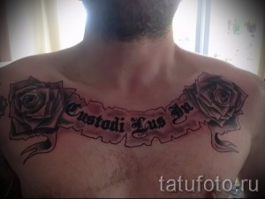 Фото тату с двумя розами и надписью 'Custodi Lus In' на груди. Черно-серые тона, детализированные цветы и лента с текстом.