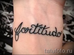 Фото тату с надписью 'Fortitude' на запястье. Черный шрифт, выполненный в каллиграфическом стиле. Простой и элегантный дизайн.