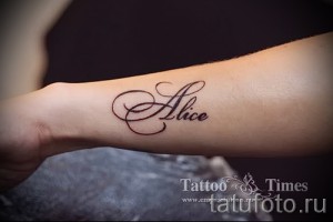 Фото тату имени «Alice» на руке. Татуировка выполнена в каллиграфическом стиле с использованием коричневых оттенков.