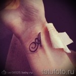 Фото тату буквы «A» на запястье. Черно-белая татуировка выполнена в минималистичном стиле с изящными завитушками.