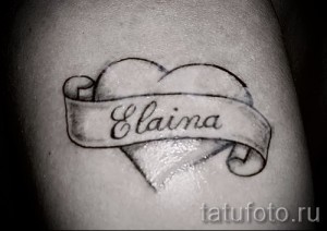 Фото тату сердца с именем «Elaina» на руке. Черно-белая татуировка выполнена в минималистичном стиле с тонкими линиями.