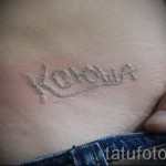Фото старой, выцветшей татуировки с надписью 'Коля' на животе, с нечеткими контурами и следами времени.