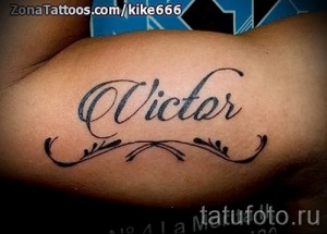 Фото татуировки с надписью 'Victor', выполненной черными и коричневыми чернилами на руке, украшенной декоративными узорами. Стильный и оригинальный рисунок татуировки.