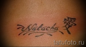 Фото тату с именем 'Nalacha', выполненным в восточном стиле, и иероглифом рядом. Татуировка на спине с использованием красных и черных чернил.