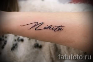 Фото минималистичной татуировки с именем 'Nikita', выполненной тонкой линией на руке. Небольшая, изящная татуировка.