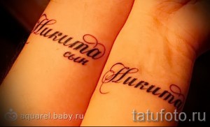 Фото парных татуировок с именем 'Nikita' и небольшим декоративным элементом, выполненных на запястьях двух людей. Нежные, красноватые татуировки.