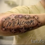 Фото тату с именем 'McKiernan', окруженным звездами, выполненное в серо-голубых тонах на бицепсе. Детализированный рисунок татуировки с эффектом объема.