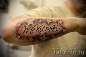 Фото тату с именем 'McKiernan', окруженным звездами, выполненное в серо-голубых тонах на бицепсе. Детализированный рисунок татуировки с эффектом объема.