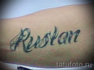 Фото тату надписи 'Rustam' на руке. Черные чернила, каллиграфический шрифт, классический дизайн. Подходит для тех, кто ценит традиционные татуировки.