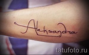 Фото тату надписи 'Aleksandra' на предплечье. Тонкие линии, каллиграфический шрифт, минималистичный дизайн. Идеально для любителей лаконичных татуировок.