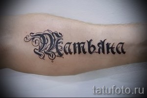 Фото тату с именем Kambaka, выполненное в готическом стиле с декоративными элементами на предплечье. Стильная татуировка для мужчин.