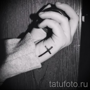 Фото тату: небольшой черный крест на руке. Минималистичный рисунок татуировки, выполненный в простом и элегантном стиле.
