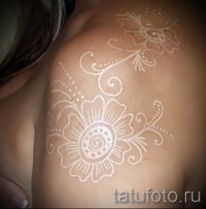 Фотография белой татуировки с изображением цветов на плече. Изящный и детализированный рисунок, выполненный в технике white ink, создает эффект нежности и элегантности.