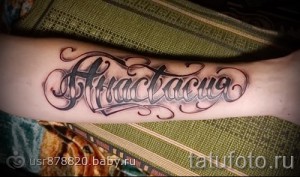 Фото тату с именем Анастасия, выполненное в стильном шрифте с тенями и контурами на предплечье. Красивый рисунок татуировки.