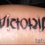 Фото татуировки с именем "Victoria", выполненным каллиграфическим шрифтом с добавлением кристаллов на коже.