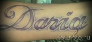 Фото татуировки с именем "Дарина", выполненным каллиграфическим шрифтом в фиолетовых и серых тонах на предплечье.