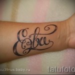 Фото татуировки с именем "Ева", выполненным изящным каллиграфическим шрифтом на запястье. Татуировка выполнена в черных тонах.