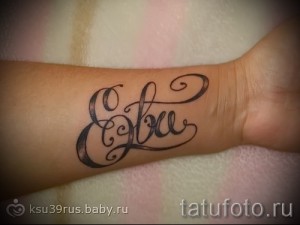 Фото татуировки с именем "Ева", выполненным изящным каллиграфическим шрифтом на запястье. Татуировка выполнена в черных тонах.