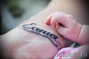 Фото тату надписи 'Евгения' с декоративными элементами на руке. Черно-серая татуировка, выполненная в классическом стиле.