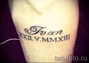 Фото тату надписи 'Иван' и даты рождения в римских цифрах на руке. Черно-серая татуировка, выполненная в классическом стиле.