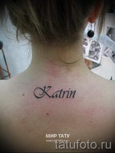 Фото тату надписи 'Katrin' изящным шрифтом на спине, чуть ниже шеи. Женственная татуировка, выполненная в черных тонах.