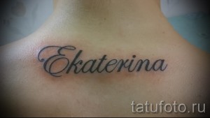 Фото тату с именем 'Ekaterina', выполненным изящным шрифтом на затылке. Черно-белая татуировка, небольшого размера.