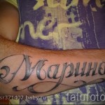 Фото тату надписи 'Марина' на предплечье, выполненной в каллиграфическом стиле с использованием черных чернил и декоративных завитков.