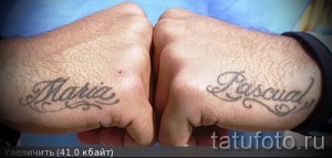 Фото парных татуировок с именами 'Maria' и 'Pascual' на тыльной стороне рук, выполненных в каллиграфическом стиле с использованием тонких линий и серого цвета.