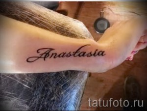 Фото тату надписи 'Anastasia' на женском запястье, выполненной в классическом стиле с тонкими линиями и коричневым оттенком.