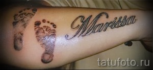 Фото тату с именем Marissa, выполненным рядом с двумя отпечатками детских ног на руке. Нежный и трогательный дизайн.