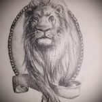 Черно-белое фото тату льва, изображенного в овальной рамке, украшенной узорами и лентой.