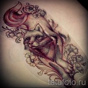 Фото эскиза татуировки лисы, лежащей среди цветущих ветвей сакуры. Рисунок выполнен в мягких, пастельных тонах и отличается высокой детализацией.