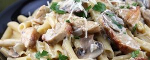 Фотография пасты с кусочками курицы, грибов и свежей зелени, посыпанной тертым сыром.
