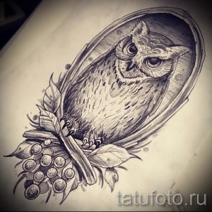 Черно-белое фото тату с изображением совы, сидящей в декоративной рамке, украшенной цветами и ягодами.