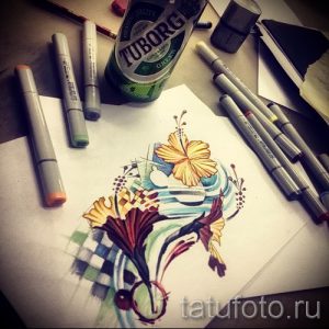 Фото тату: эскиз цветка в стиле олд скул, с использованием ярких цветов и четких контуров. Рядом с рисунком лежат маркеры и банка.