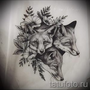 Красивый эскиз татуировки с изображением трех лисьих голов, окруженных цветами и листьями. Рисунок выполнен в технике графики, с высокой детализацией и мягкими линиями.
