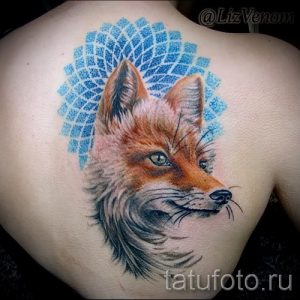 Фото реалистичной татуировки головы лисы на плече, с детально прорисованной шерстью и выразительными глазами на фоне голубого круга.