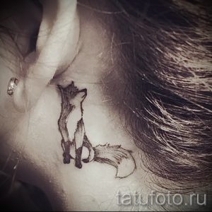 Фото миниатюрной татуировки лисы за ухом. Рисунок выполнен в технике blackwork, с четкими линиями и минимальным количеством деталей.