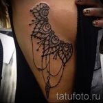 Фотография коричневой татуировки совы, стилизованной под мандалу, на бедре девушки. Детализированный рисунок с геометрическими узорами и точками.