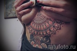 Фото тату: красивая мандала в пастельных тонах украшает грудь девушки. Детализированный рисунок татуировки с тонкими линиями и нежными оттенками.