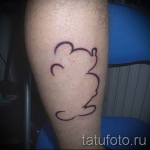 Фото тату на икре: контурный рисунок головы Микки Мауса, выполненный черными линиями, без заливки и теней.