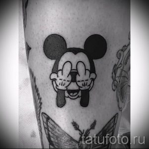 Фото татуировки Микки Мауса, показывающего средний палец. Черно-белый рисунок татуировки, выполненный в мультяшном стиле.
