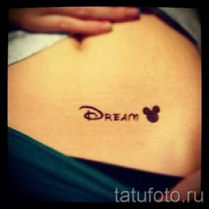 Фото минималистичной татуировки с надписью 'DREAM' и силуэтом головы Микки Мауса. Черно-белый рисунок татуировки, выполненный в лаконичном стиле.