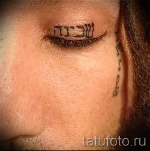 Фото татуировки на бровной дуге: ивритский текст. Небольшая татуировка, выполненная черными чернилами.