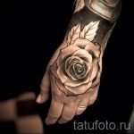 Фото тату: реалистичная татуировка розы на руке. Черно-серые тона, детализированный рисунок, листья и стебель.