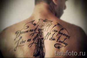 Фото тату на спине с изображением пера и надписью 'Dream as if you'll live forever. Live as if you'll die today'. Черно-белый рисунок.