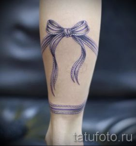Фото тату: фиолетовый бант с ниспадающими лентами на запястье. Детализированный рисунок татуировки, выполненный в мягких тонах, подчеркивает женственность и изящество.