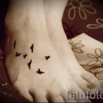 Фото тату на стопе: стая маленьких птиц, летящих в одном направлении. Минималистичный и элегантный рисунок татуировки.