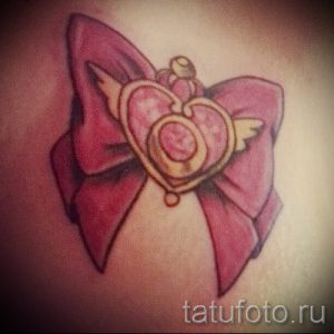 Фото тату розового бантика с сердцем и крыльями на руке. Яркий и привлекательный рисунок татуировки.