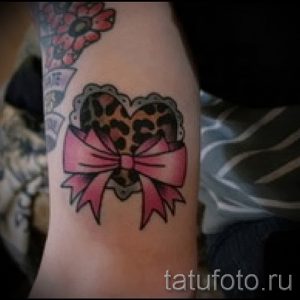 Фото тату сердца с леопардовым принтом, украшенного розовым бантиком на руке. Яркий и привлекательный рисунок татуировки.